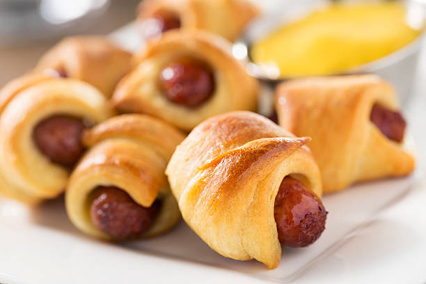 Close-up of mini crescent rolls filled with sausages, served on a plate with mustard in the background.