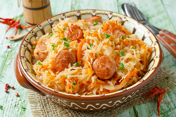 A bowl of traditional sauerkraut with sausages and carrots on a rustic table