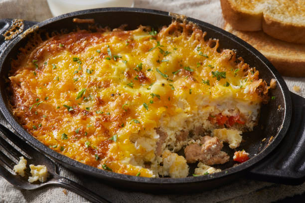 A delicious casserole topped with melted cheese and herbs served in a cast iron dish, alongside slices of toasted bread.