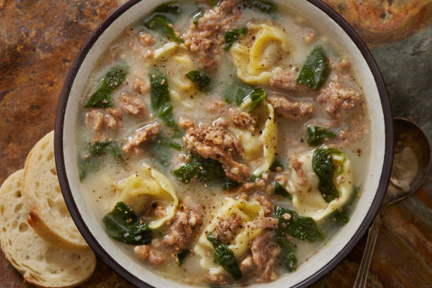 A bowl of creamy tortellini soup with spinach and sausage, accompanied by slices of bread.