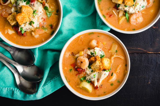 Three bowls of creamy shrimp soup garnished with herbs and croutons on a teal fabric background.