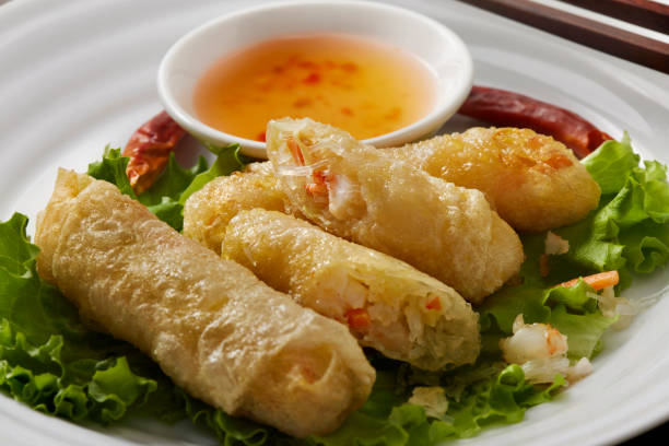 A plate of crispy spring rolls served on a bed of lettuce with a side of dipping sauce.