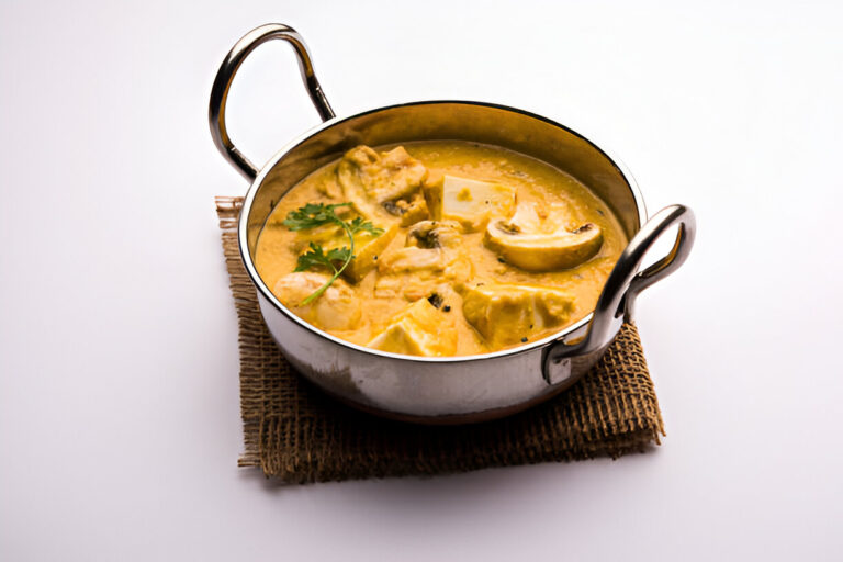 A bowl of creamy curry with tofu and vegetables garnished with coriander on a burlap mat.