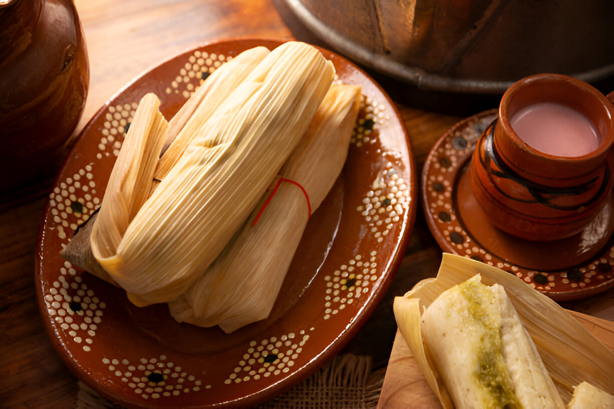 A plate of tamales with a traditional clay cup of drink on a wooden table.