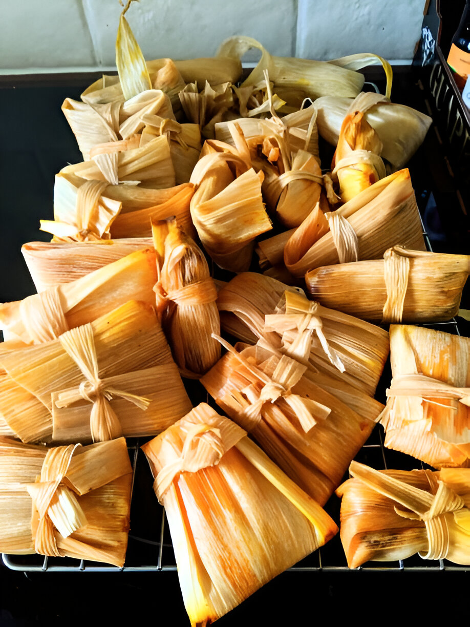 A collection of wrapped food items made from corn husks and tied with string, sitting on a wire rack.