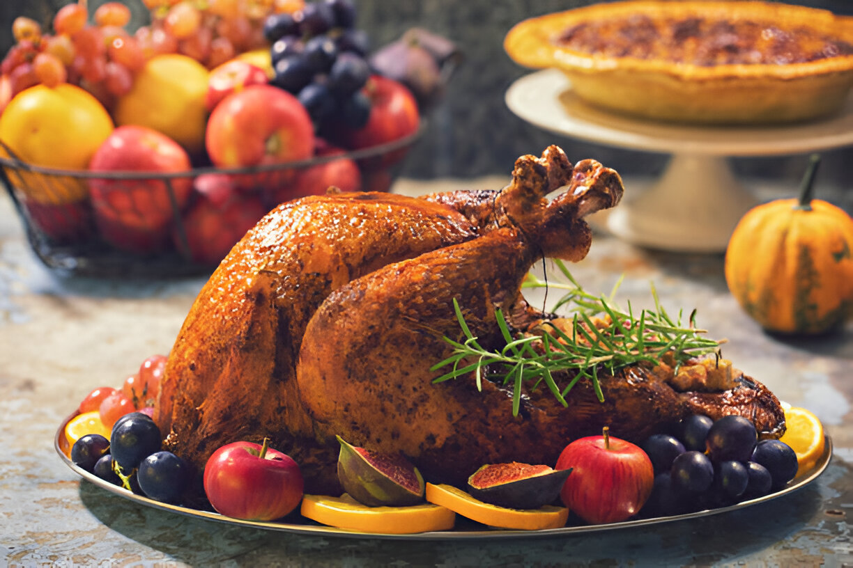 A beautifully roasted turkey on a platter with fruits and herbs, decorated for a festive meal.