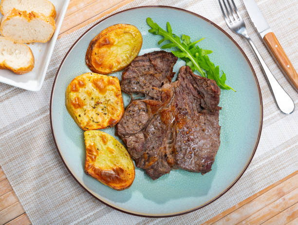 A plate of grilled steak accompanied by roasted potatoes and fresh arugula on a textured table setting.