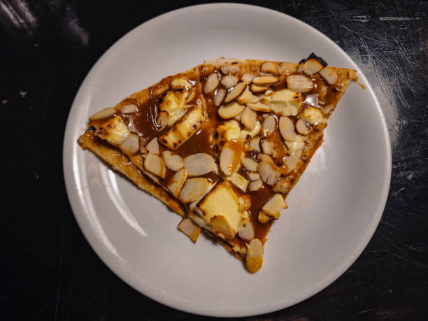 A slice of dessert topped with almond slivers and a glossy caramel layer, served on a white plate.