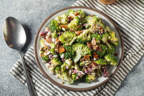 A plate of fresh broccoli salad topped with chopped bacon, onions, and nuts, served on a striped cloth.