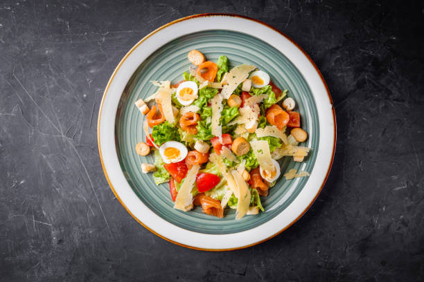 A fresh salad served on a decorative plate with greens, tomatoes, pasta pieces, and cheese shavings.