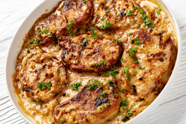 A delicious plate of juicy pork chops in a creamy sauce, garnished with fresh parsley.