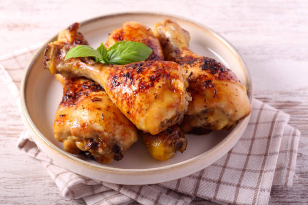 A plate of grilled chicken drumsticks garnished with basil leaves