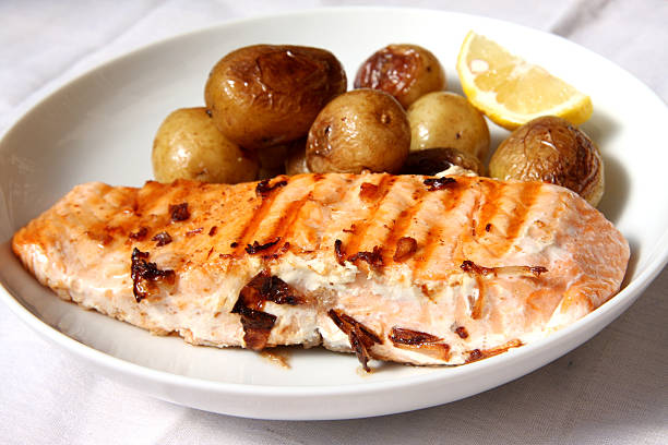 A plate of grilled salmon fillet served with roasted baby potatoes and a lemon wedge.