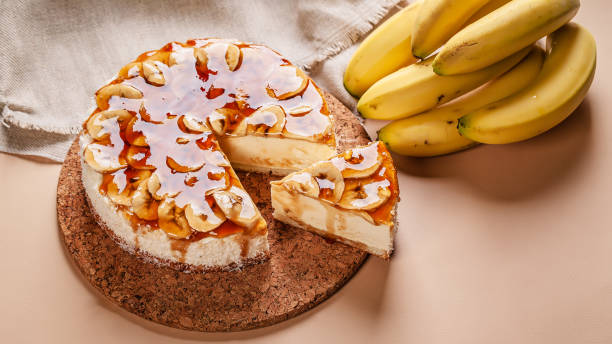 A delicious banana cheesecake with a slice removed, served with fresh bananas on the side.