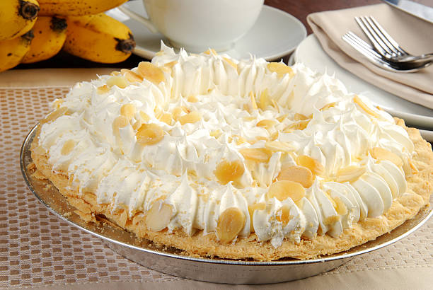 A delicious banana cream pie topped with whipped cream and almond slices, with bananas in the background.