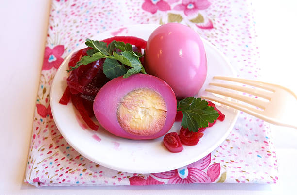 A plate with pink eggs, sliced to show the inside, garnished with green leaves and accompanied by slices of red beets, resting on a floral napkin.