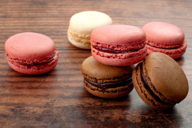 A variety of macarons including pink, red, white, and brown placed on a wooden surface.