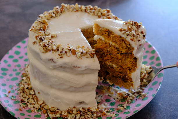 A layered carrot cake with cream cheese frosting and chopped nuts on a colorful polka dot plate, with a slice removed.