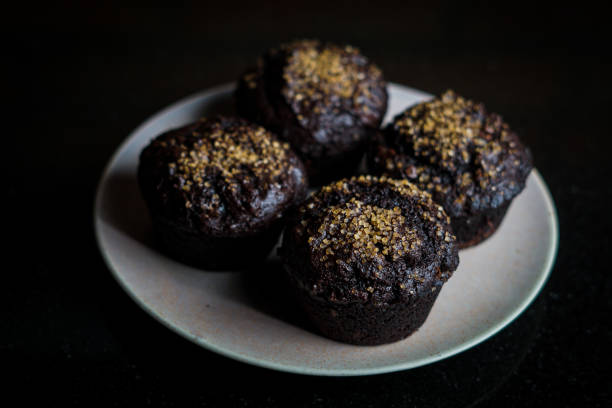 A plate of four dark chocolate muffins topped with sparkling sugar crystals.