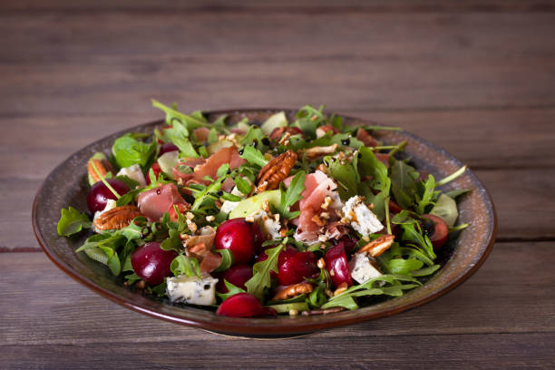 A colorful salad featuring greens, grapes, nuts, and cheese in a bowl on a wooden table.