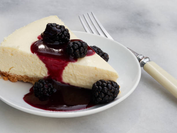 A slice of cheesecake topped with blackberries and berry sauce on a white plate with a fork beside it.