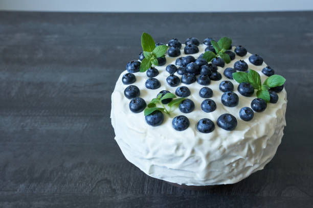 A round cake topped with fresh blueberries and mint leaves on a dark wooden surface.