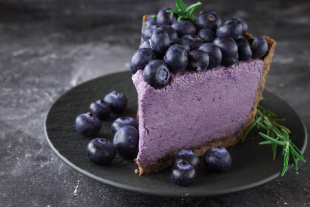 A slice of blueberry cheesecake topped with fresh blueberries on a black plate.