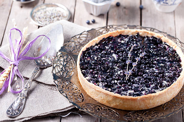 A blueberry tart placed on a decorative plate surrounded by serving utensils.