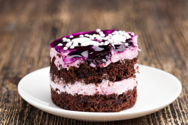 A slice of chocolate cake with purple berry icing and white sprinkles on a white plate