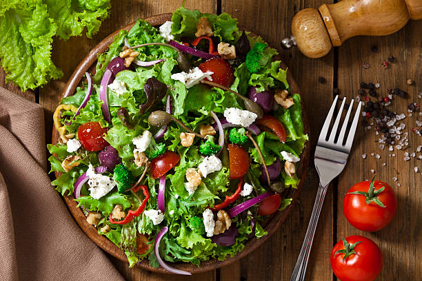 Fresh vegetable salad with tomatoes, olives, broccoli, and feta cheese on a wooden plate