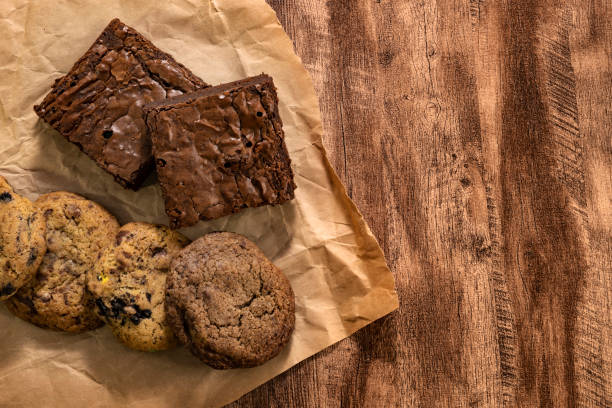 A top view of assorted baked goods including brownies and various cookies on crumpled brown paper.