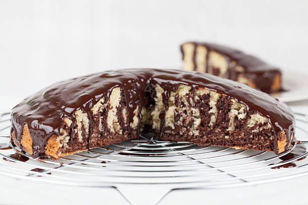 A chocolate cake with a marbled interior, partially sliced, placed on a wire cooling rack.