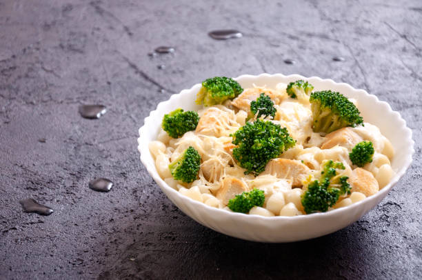 A bowl of pasta with broccoli and cheese on a dark textured surface