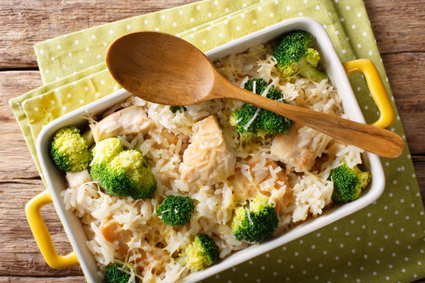 A dish of chicken and broccoli rice casserole topped with melted cheese, served in a white baking dish with a wooden spoon.