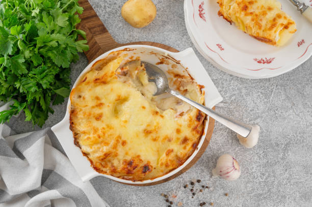 A freshly baked potato gratin in a white dish, surrounded by fresh herbs and kitchen ingredients.