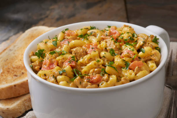 A bowl of creamy pasta with cheese, herbs, and diced tomatoes, accompanied by slices of toasted bread.