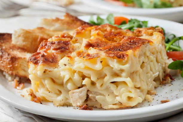 A delicious serving of creamy baked chicken pasta with a crispy top and garlic bread on the side.