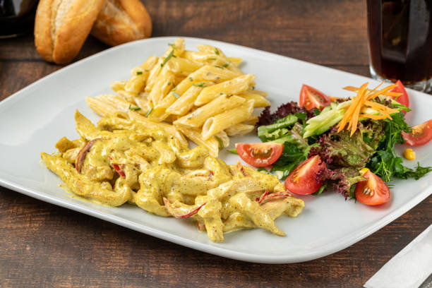 A plate of pasta with a creamy sauce, accompanied by a side salad and bread rolls.