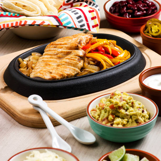 Sizzling chicken fajitas served on a hot skillet with colorful peppers and onions, accompanied by guacamole, beans, tortillas, and sour cream.