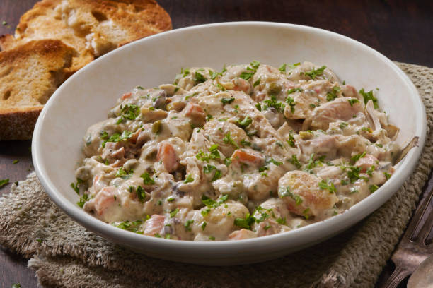 A creamy dish with shrimp, vegetables, and herbs served in a white bowl alongside toasted bread.