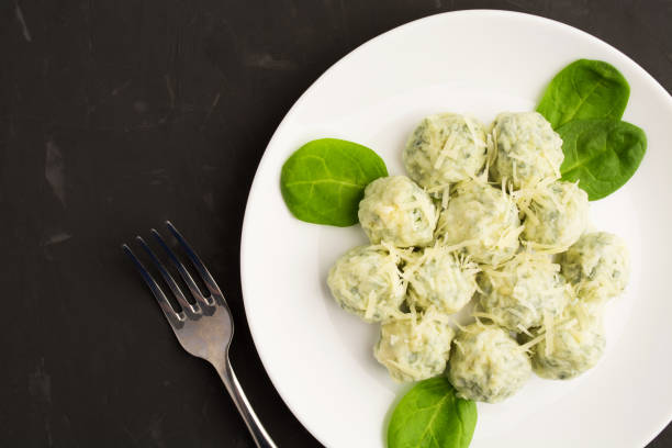 A plate of spinach dumplings topped with grated cheese and fresh spinach leaves on a black surface.