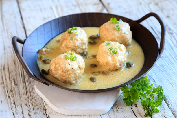 A black skillet containing four meatballs in a creamy sauce, garnished with parsley.