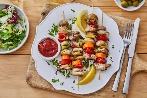 Grilled chicken and vegetable skewers served on a white plate with a side of ketchup and lemon slices.