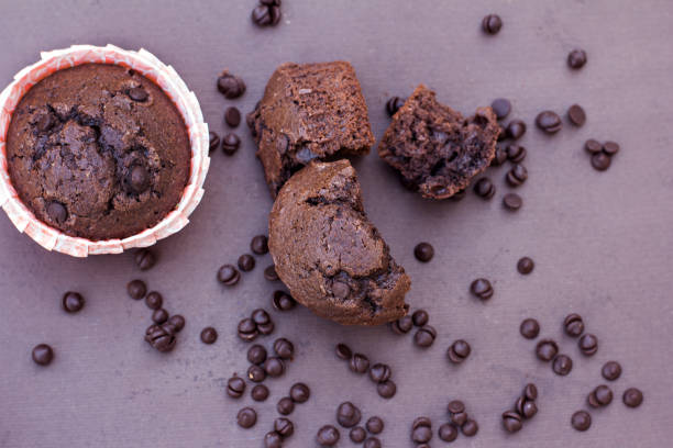 A freshly baked chocolate muffin with chocolate chips, surrounded by chocolate chips on a dark surface.