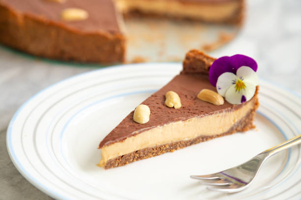 A slice of chocolate peanut butter pie on a white plate, garnished with a purple flower and peanuts.