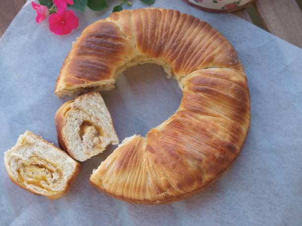 A golden-brown ring-shaped pastry with a slice cut out showing its fluffy interior, placed on a parchment paper background.