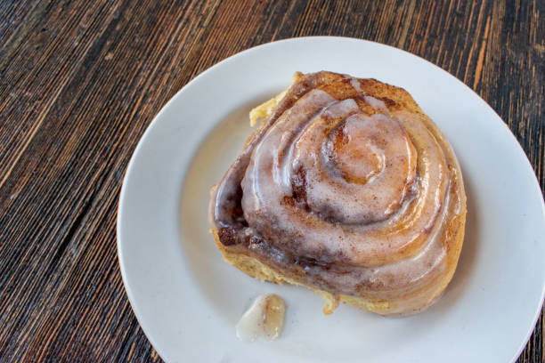 A delicious cinnamon roll drizzled with icing on a white plate