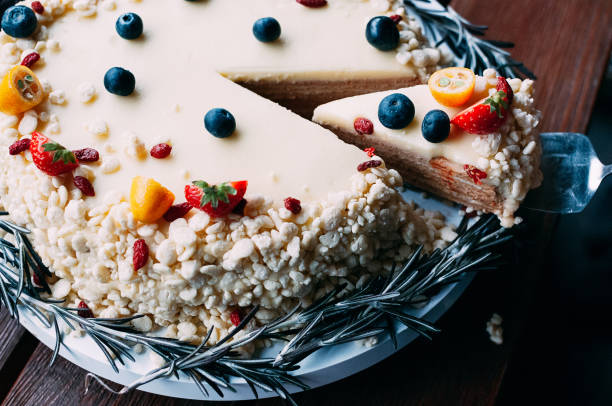 A beautifully decorated cake with a slice removed, garnished with fresh fruit and nuts.