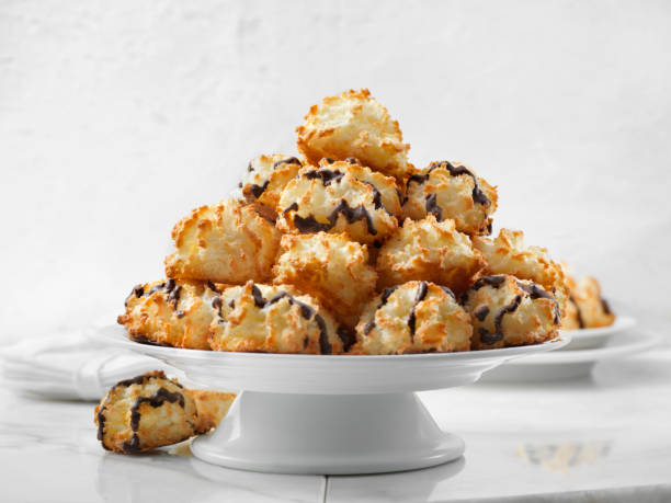 A large pile of coconut macaroons drizzled with chocolate on a white pedestal plate.