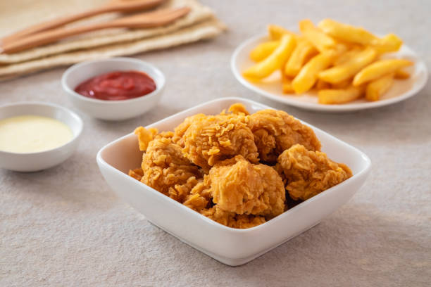 A bowl of crispy fried chicken pieces served with dipping sauces and fries.